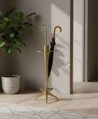 Gold umbrella stand with a plant and open umbrella in a room with wooden floor and white walls.