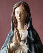 Statue of a woman in a blue hood with hands clasped, on a brown background