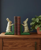Decorative bookends shaped like rabbits on a wooden surface with a plant in the background.