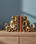 Gold octopus bookends on a wooden surface with a plant and books against a blue wall.