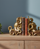 Gold octopus bookends holding books on a wooden surface with a plant in the background.