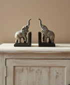 Decorative elephant bookends on a wooden cabinet with a plant in the background.