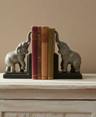 Elephant bookends holding books on a wooden surface with a beige wall background