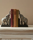 Elephant bookends holding books on a wooden surface with a beige wall background