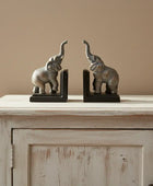Bronze elephant bookends on a wooden cabinet against a beige wall