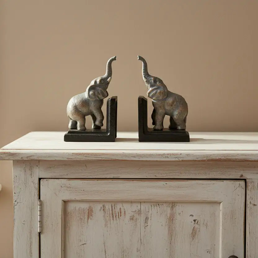 Bronze elephant bookends on a wooden cabinet against a beige wall