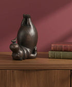 Bronze sculpture of a cat and mouse on a wooden surface with books against a red background