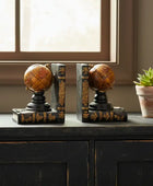 Decorative bookends with globe design on a wooden surface near a window.