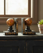 Decorative bookends shaped like globes on a wooden surface with a potted plant in the background.