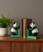 Panda bookends on a wooden surface with books and a plant in the background