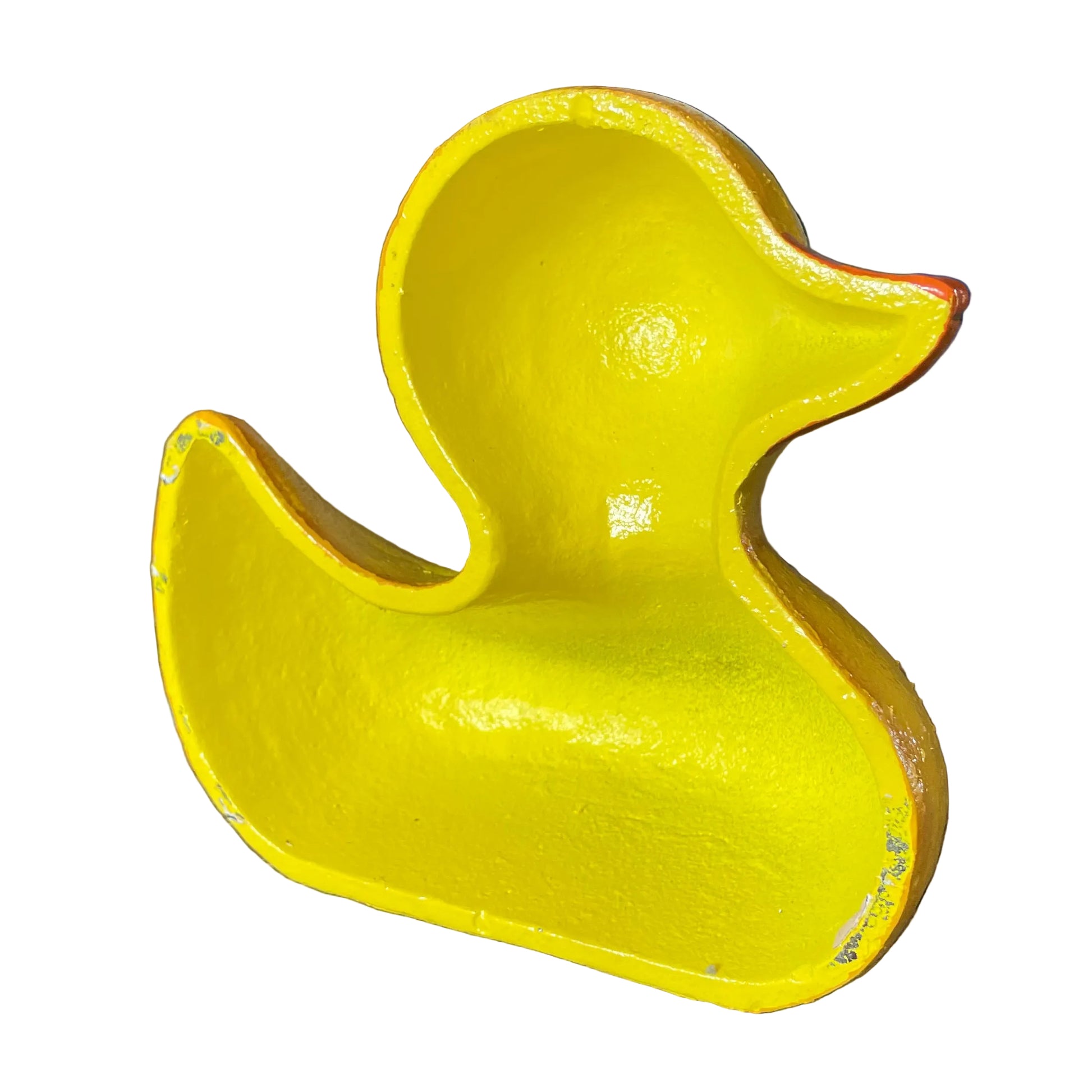 A bright yellow duck-shaped container or tray with a glossy finish, photographed in a warehouse-like setting on a cardboard surface.
