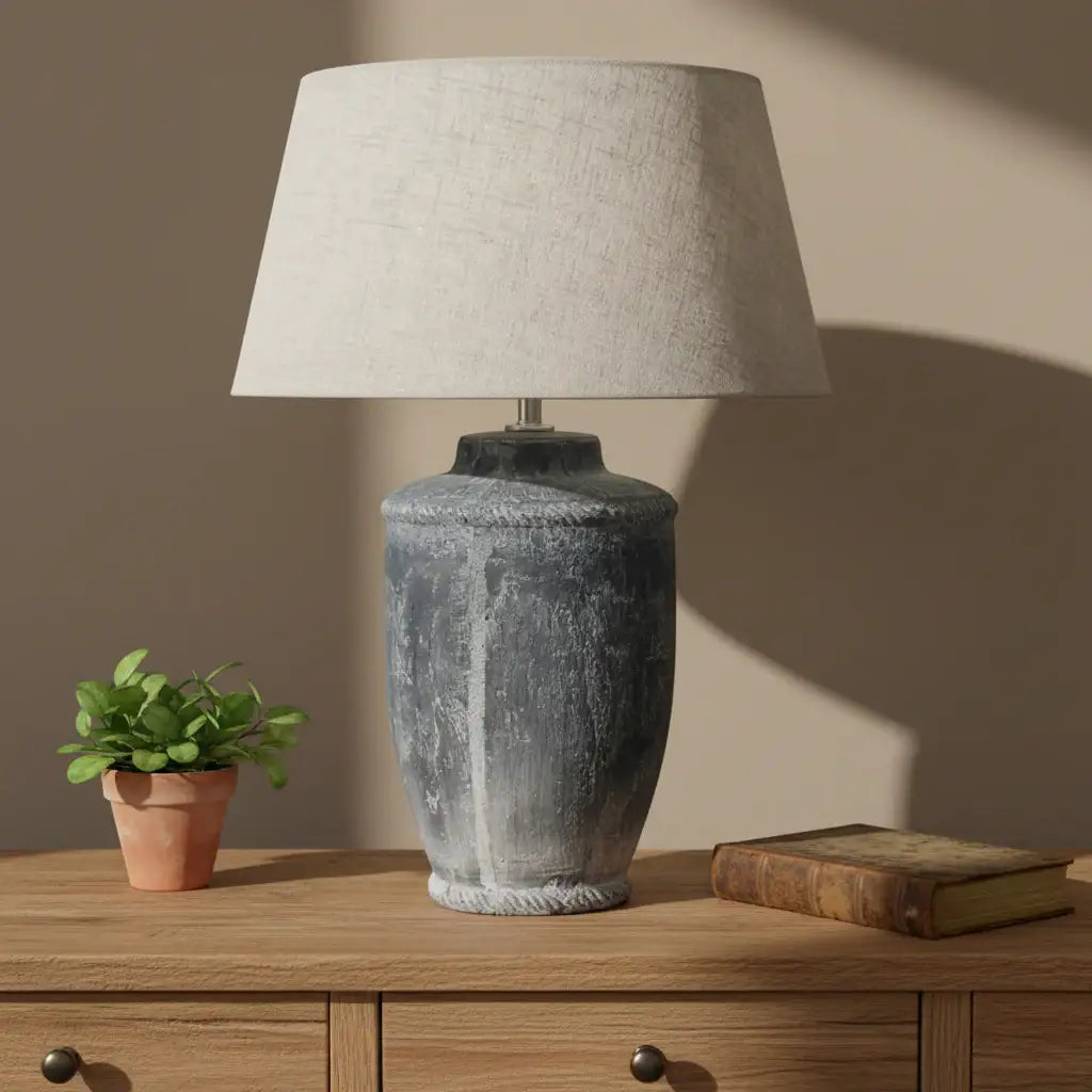 Decorative lamp with textured base and beige shade in a room setting with framed artwork and mugs.