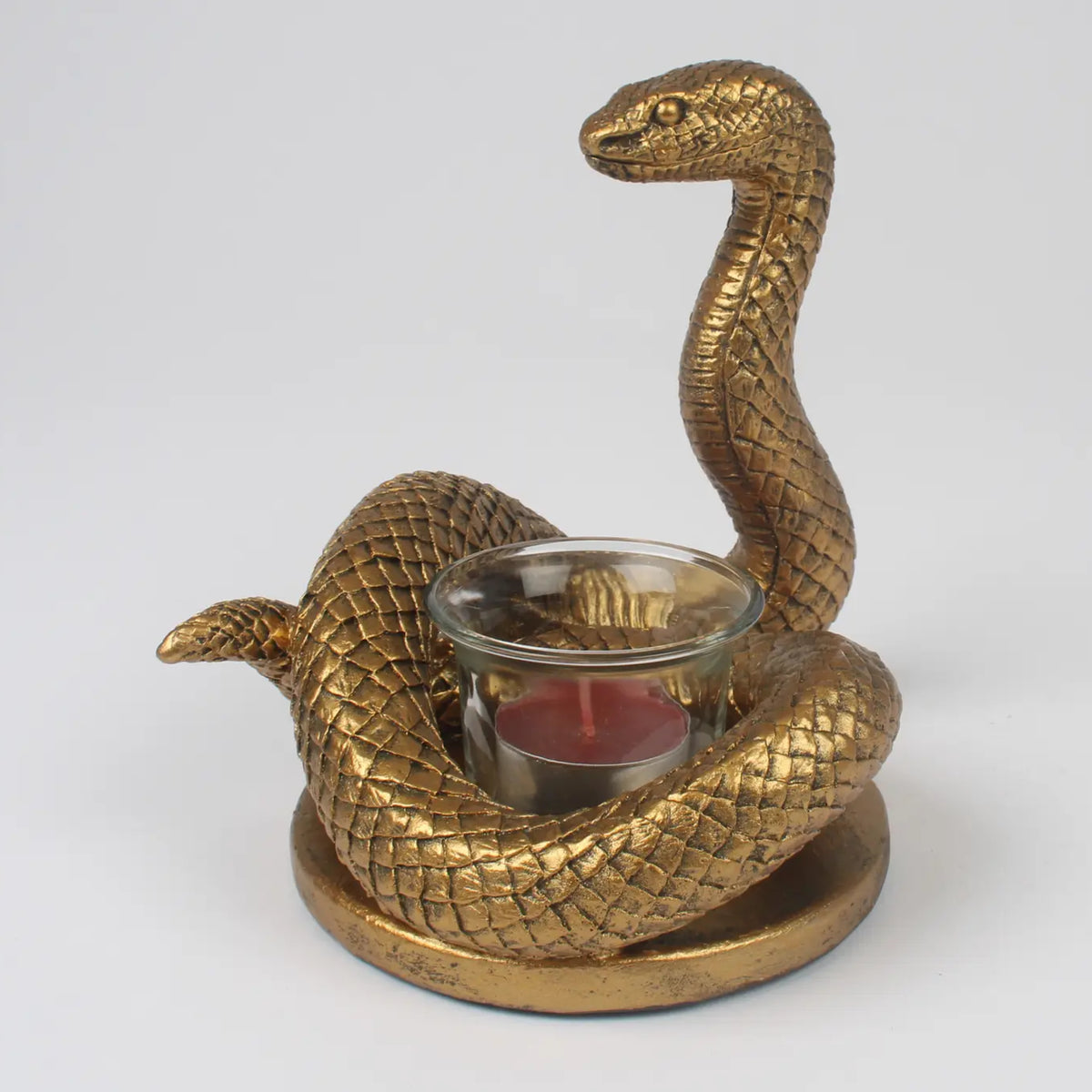 A gold-finished snake-shaped candle holder with a glass candle holder in the center containing a red candle, set against a plain light gray background.