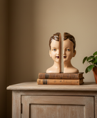 Bookend shaped like a boy's head on a wooden cabinet with a plant