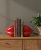 Red lip-shaped bookends on a wooden surface with books and a plant.