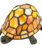A stained-glass tortoise figurine with a mosaic shell in shades of yellow, orange, and white, separated by dark metal grout lines, on a plain white background.