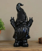 Black gnome figurine making peace signs on a wooden surface with a plant and book in the background.