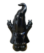 Black ceramic gnome figurine with a long hat on a wooden surface with a stone wall background