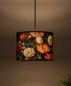 A hanging drum lampshade with a dark floral tapestry pattern featuring red, yellow, and cream flowers, suspended by a black cord against a warm brown background.