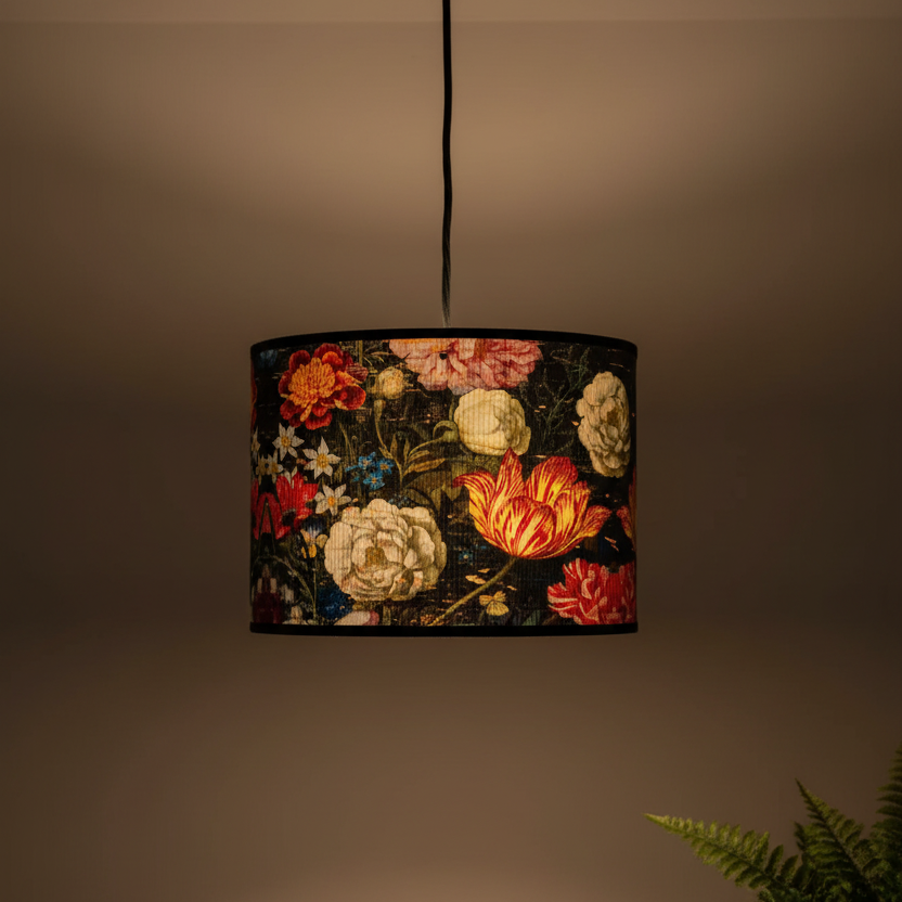 A hanging drum lampshade with a dark floral tapestry pattern featuring red, yellow, and cream flowers, suspended by a black cord against a warm brown background.