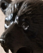 Close-up of a dark cast-iron bear head container or decor piece, showing textured fur details and a glossy finish against a neutral beige background.