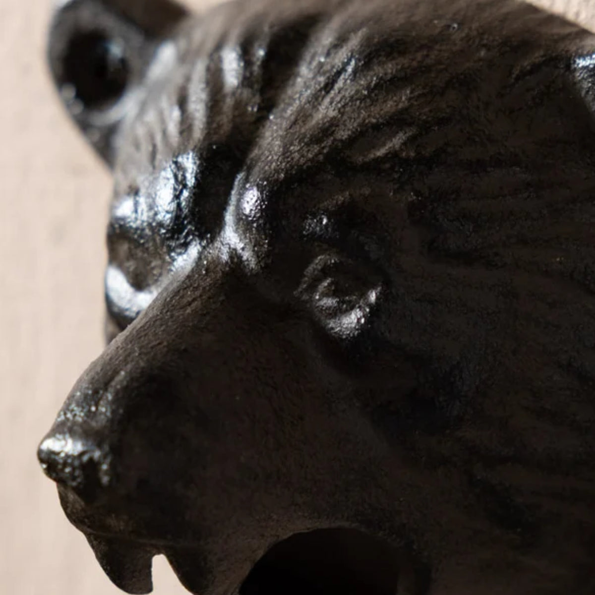 Close-up of a dark cast-iron bear head container or decor piece, showing textured fur details and a glossy finish against a neutral beige background.