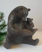 Bronze statue of a bear reading a book to a cub with a Christmas tree in the background