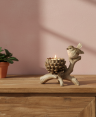 Decorative candle holder with a bird figurine on a wooden surface next to a potted plant.
