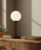 Table lamp on a wooden surface with a plant and book in a room with natural light.