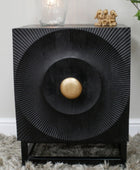 Decorative black side table with a gold ball in the center, placed on a textured surface.