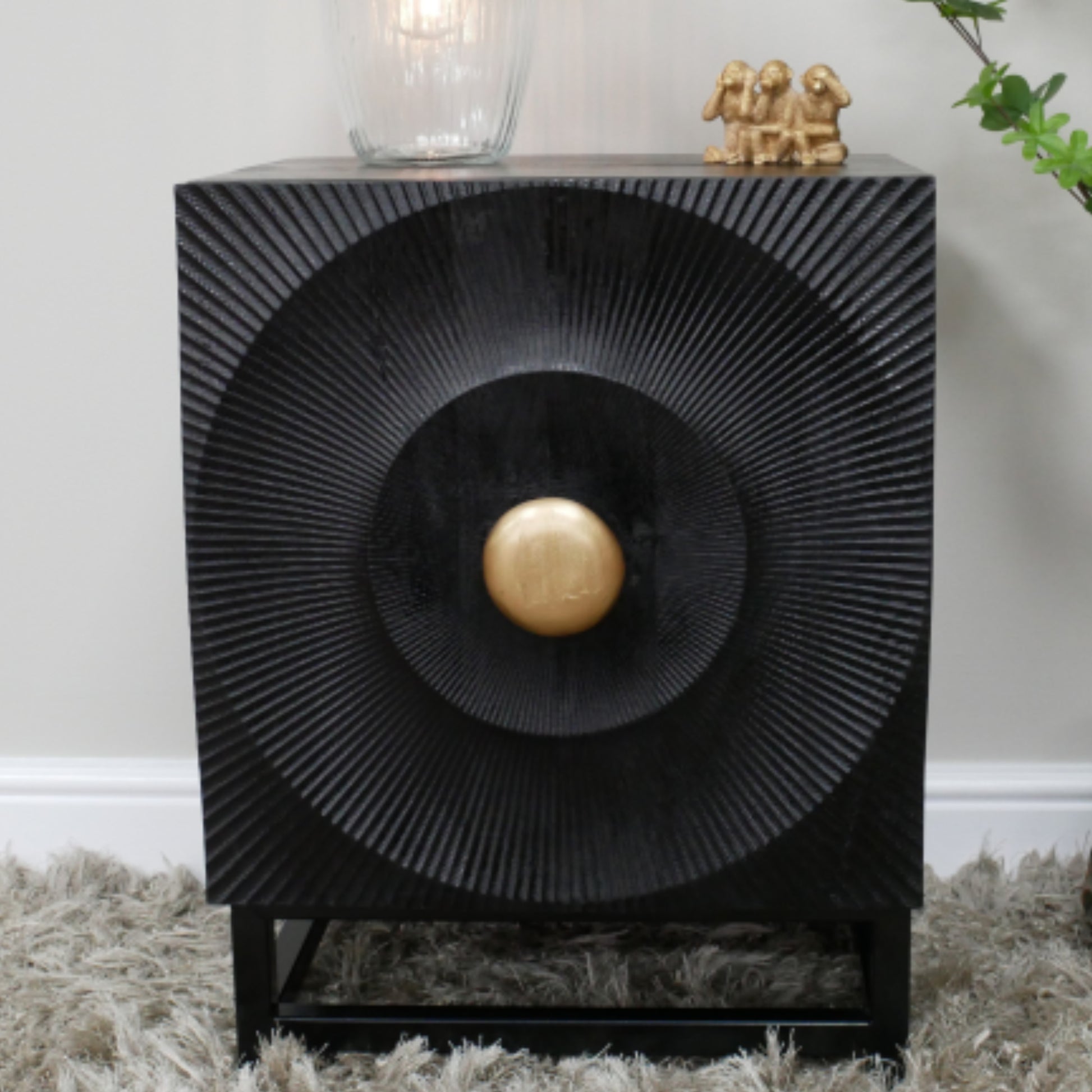 Decorative black side table with a gold ball in the center, placed on a textured surface.