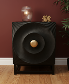 Decorative black speaker with gold center on a wooden floor against a red wall.