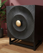 Decorative black speaker with gold center on a wooden floor against a red wall.