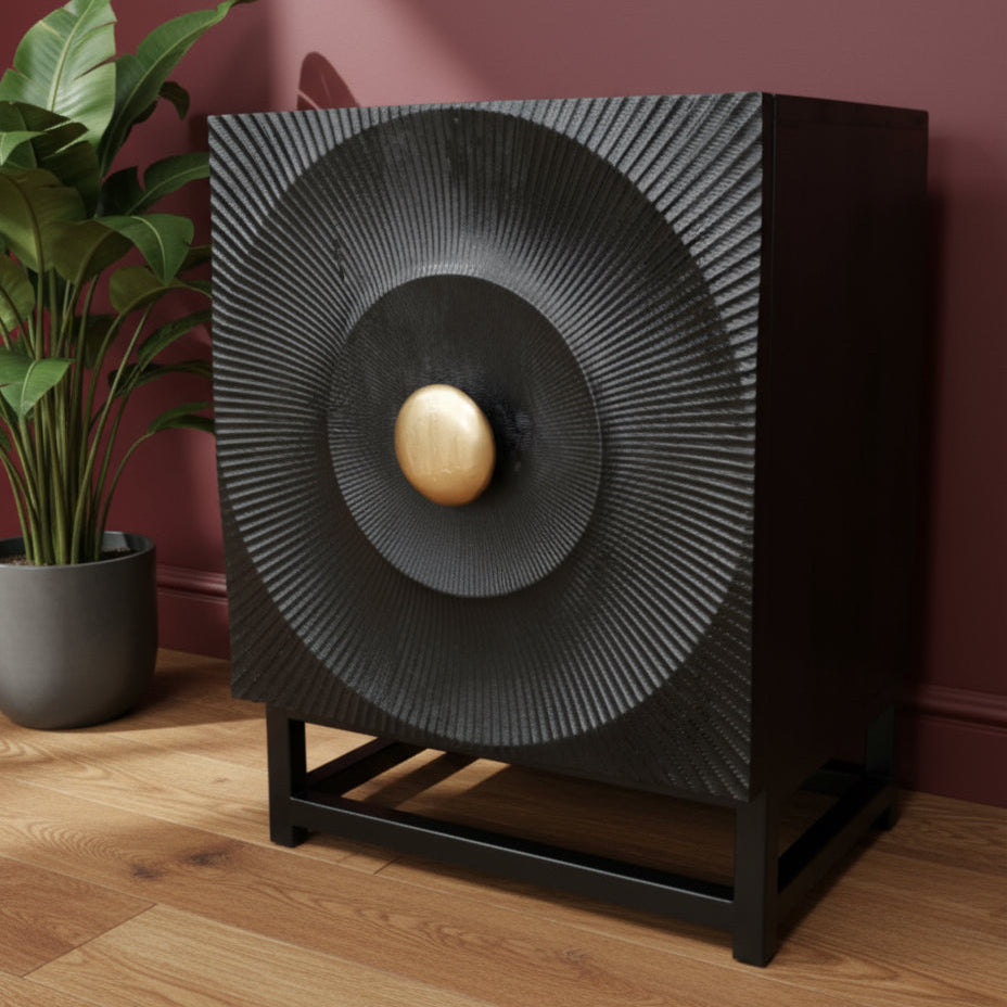 Decorative black speaker with gold center on a wooden floor against a red wall.