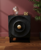Black decorative cabinet with gold ball on a wooden floor against a pink wall.
