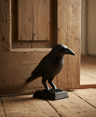 Decorative crow figure on a wooden floor with a wooden door in the background