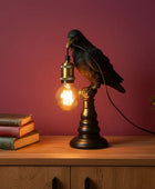 Decorative bird lamp on a wooden surface with books and a plant against a purple wall.