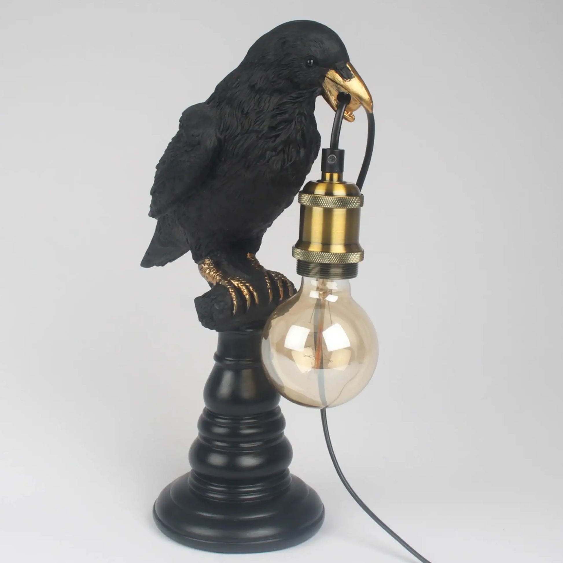 Black bird-shaped lamp with a gold beak holding a light bulb on a white background