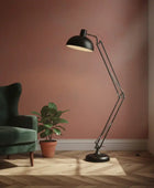 Black floor lamp in a room with a green armchair and plant on a wooden floor.