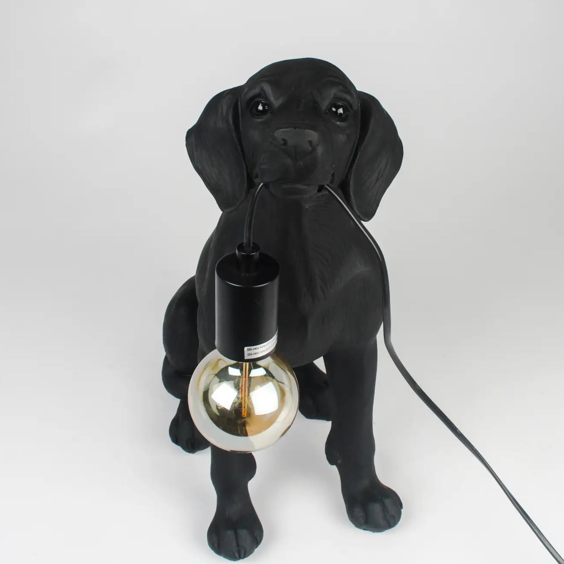 Black dog-shaped lamp holding a light bulb on a white background