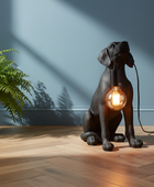 Dog-shaped lamp with a lit bulb on a wooden floor next to a plant.