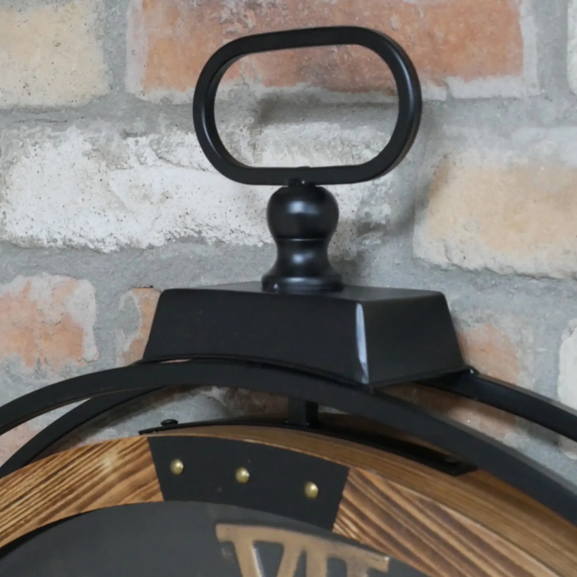 Close-up of a black and wooden clock against a brick wall.
