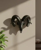Decorative black ram's head wall mount on a beige wall with a plant in the foreground.