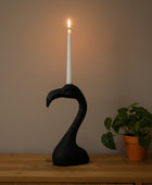 Black flamingo-shaped candle holder with a lit candle on a wooden surface.