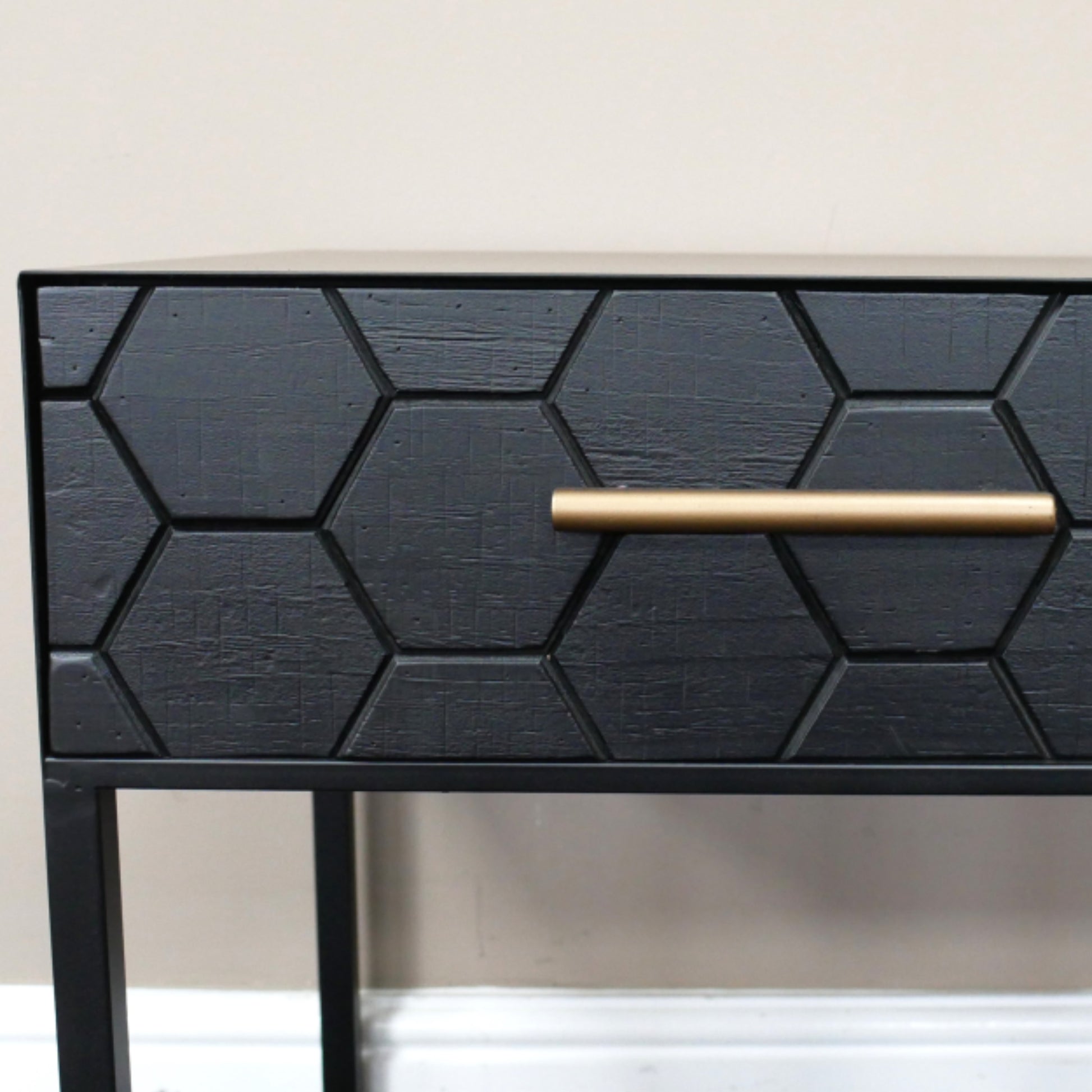 Black geometric-patterned side table with a gold handle on a neutral background