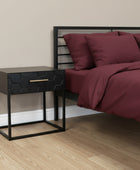 Black geometric-patterned side table with a gold handle on a gray surface.