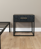 Black hexagonal patterned nightstand with a gold handle on a wooden floor.