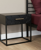 Black hexagonal patterned nightstand with gold handle next to a bed with burgundy bedding.