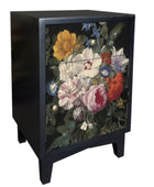 A black wooden side table or cabinet with two drawers, featuring a detailed floral print on the front doors. The flowers include yellow, white, pink, red, and blue blossoms with green leaves, set against a dark background.