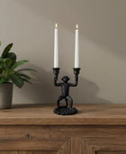 Black monkey-shaped candle holder with two lit white candles against a blue background